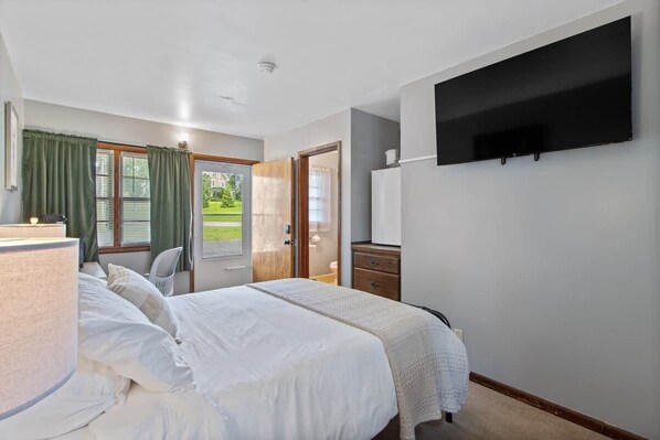 A bedroom with a bed, a flat-screen TV, a dresser, a chair, and a door leading to a balcony.