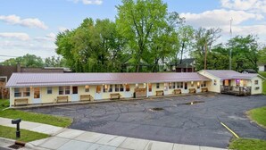 Un motel composé d’une rangée de chambres, d’un parking et d’un petit bâtiment doté d’une véranda.