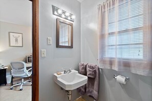 A bathroom with a sink, mirror, towel rack, and window with blinds.