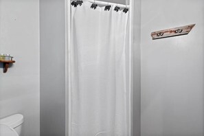 A bathroom with a white shower curtain, a wooden shelf with toiletries, and a wall-mounted towel rack.