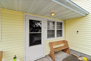 A yellow house with a white door, two windows, a bench, and a small potted plant.