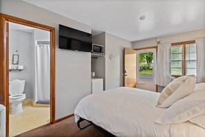 A bedroom with a bed, a television, a door leading to a bathroom, and a window with curtains.