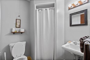 A bathroom with a toilet, shower curtain, sink, and a shelf with toiletries.