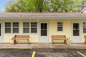 A single-story building with numbered doors, two benches outside, and a small table with a plant.
