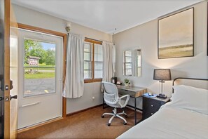 A hotel room with a bed, desk, chair, and a view of a motel sign outside.