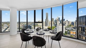 Une chambre située dans un immeuble de grande hauteur, offrant une vue panoramique sur la ville, avec une table à manger ronde entourée de chaises et une grande fenêtre.