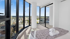 Une chambre située dans un immeuble de grande hauteur, avec vue sur la ville, de grandes fenêtres, un lit agrémenté d’un tapis moelleux et une serviette blanche.