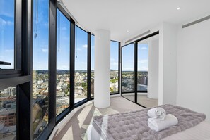 Ein Schlafzimmer in einem Hochhaus mit Blick auf die Stadt, großen Fenstern, einem Bett mit flauschigem Teppich und einem weißen Handtuch.