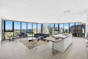 A modern living room with a large window, a sofa, a dining table, and a kitchen area. - LUXE PENTHOUSE | 3BR w/ Panoramic Story Bridge, Brisbane River and City Views (Fortitude Valley)