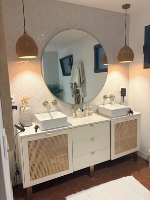 Une salle de bain avec un meuble-lavabo à deux vasques, un miroir rond, deux lampes suspendues et un tapis blanc.