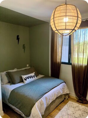 Une chambre à coucher avec un lit, un luminaire suspendu, une fenêtre avec des rideaux et un interrupteur fixé au mur.