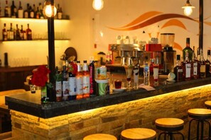 Una zona de bar con mostrador de piedra, taburetes y diversos botellas y vasos.