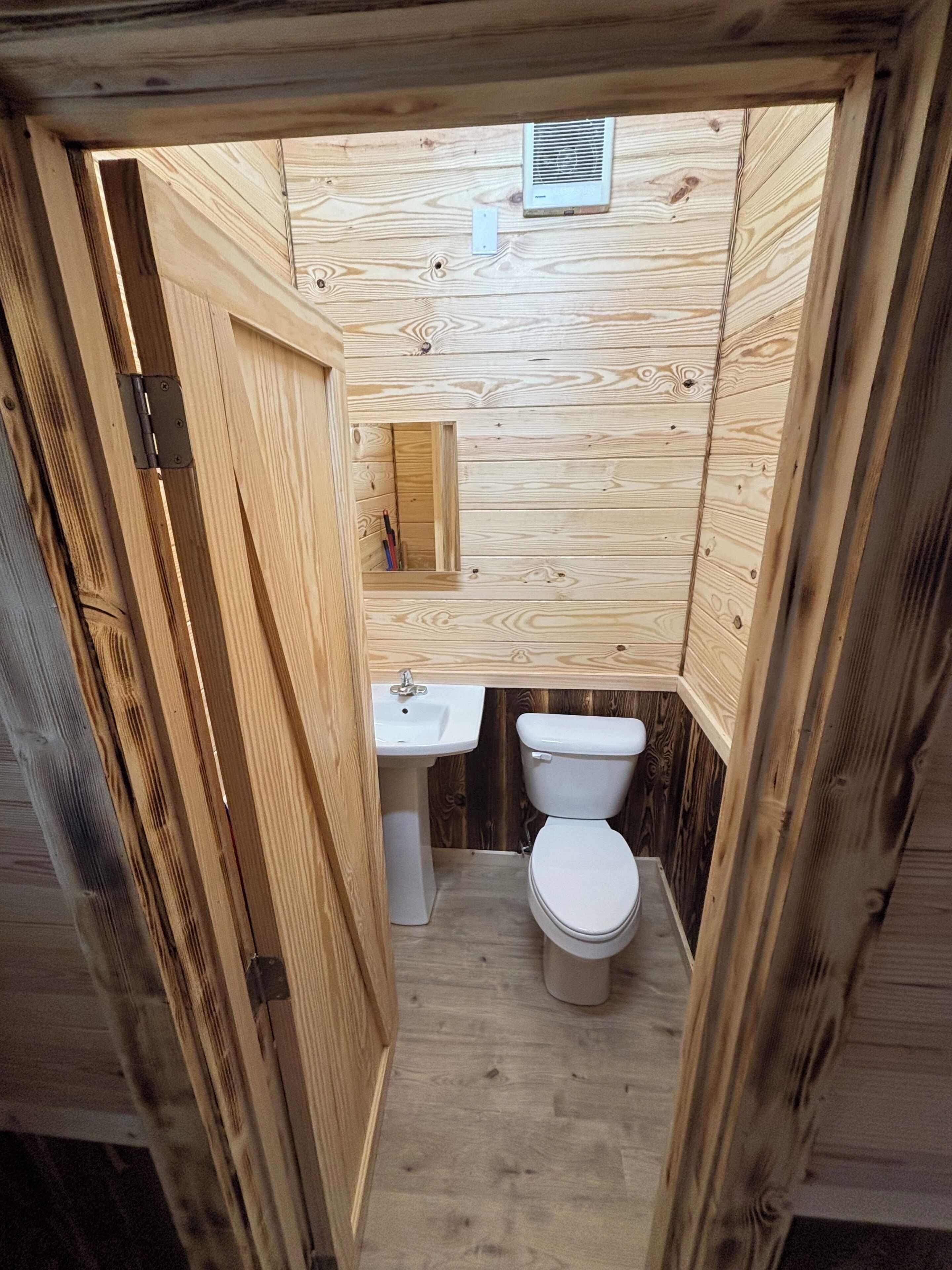 Ein kleines, kompaktes Badezimmer aus Holz mit Waschbecken, Toilette und einem kleinen Spiegel.