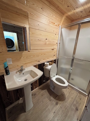 A wooden-paneled bathroom with a sink, toilet, and glass shower enclosure.