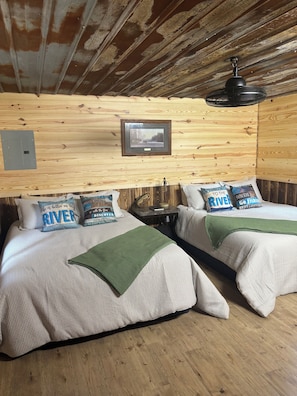 A cabin-style room with two beds, a framed picture on the wall, and a ceiling fan.