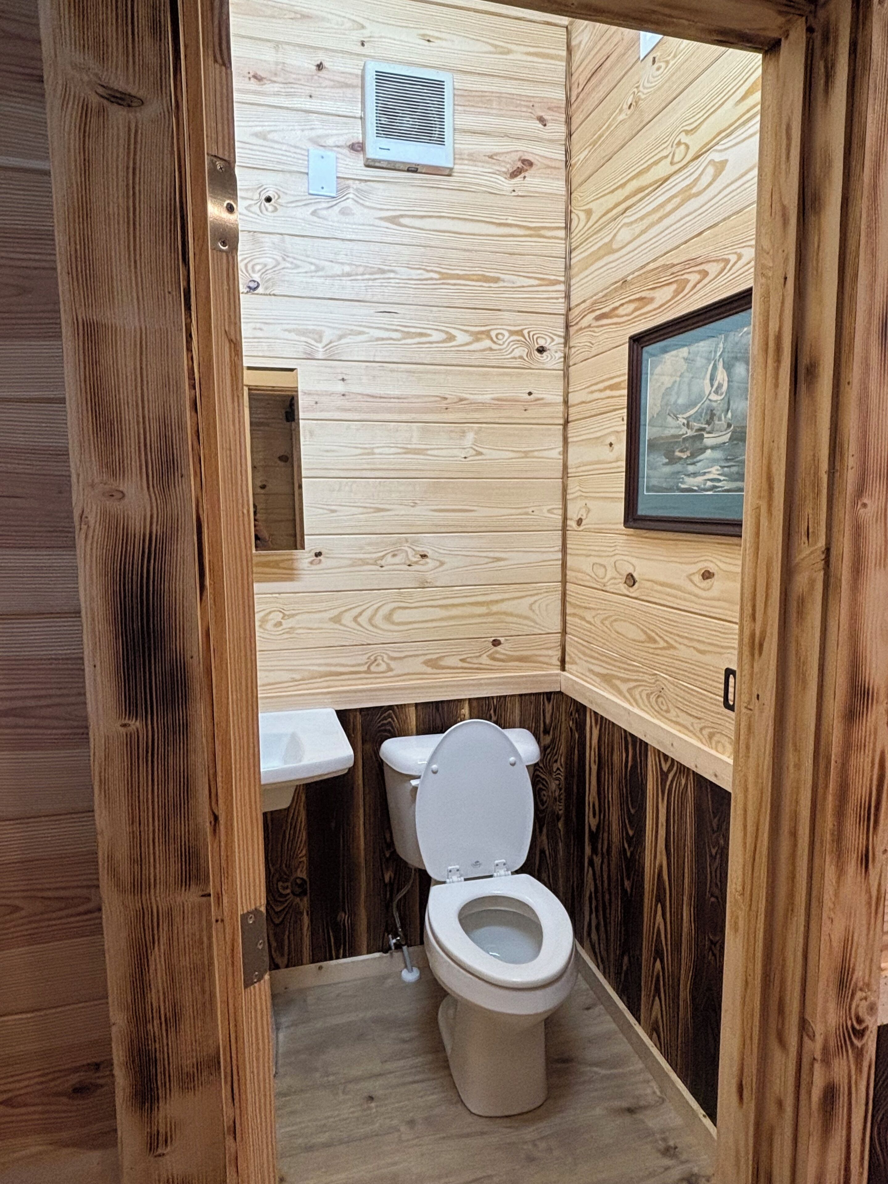 Un baño con paneles de madera, un inodoro, un lavabo y una obra de arte enmarcada en la pared.