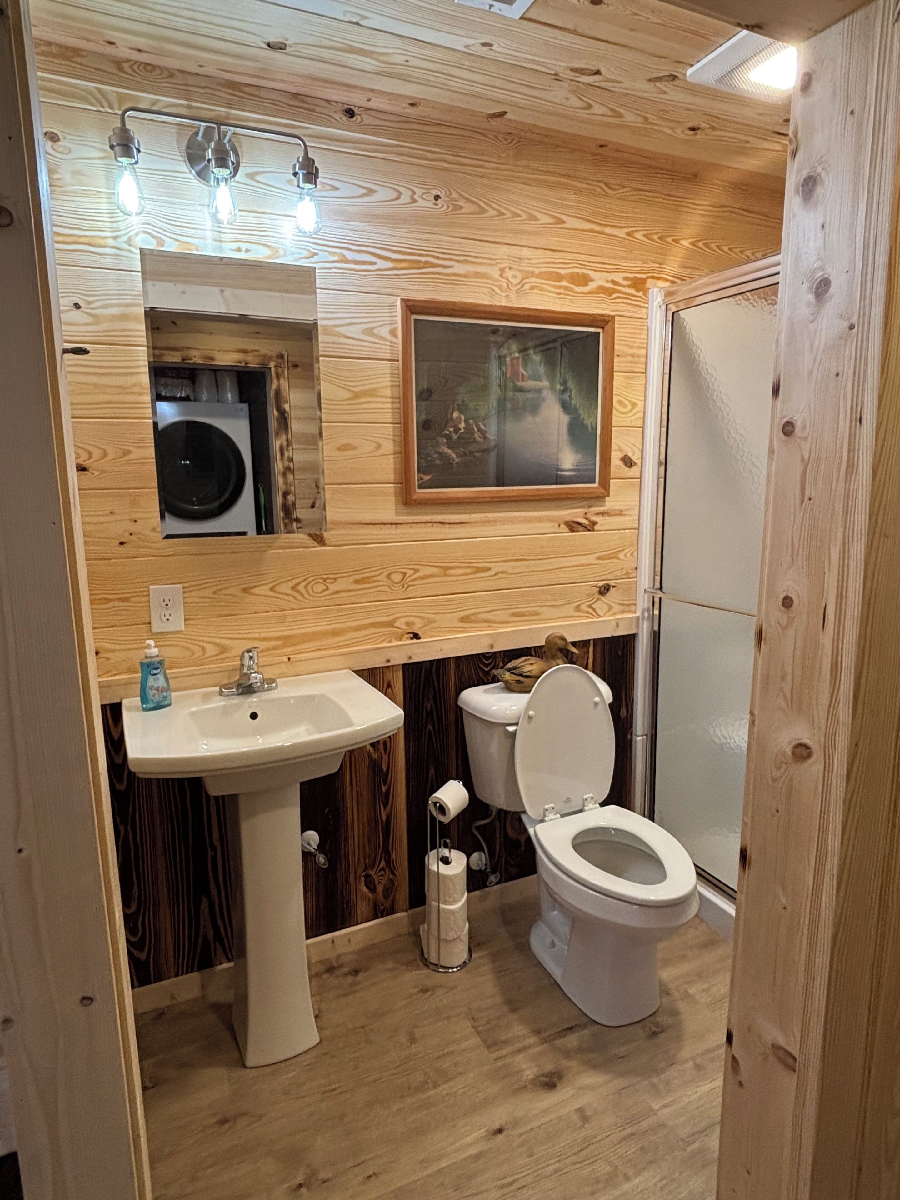 Ein Badezimmer mit Holzwandverkleidung, einem Waschbecken, einer Toilette und einer Dusche.