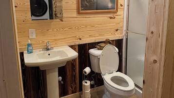 Ein Badezimmer mit Holzwandverkleidung, einem Waschbecken, einer Toilette und einer Dusche.