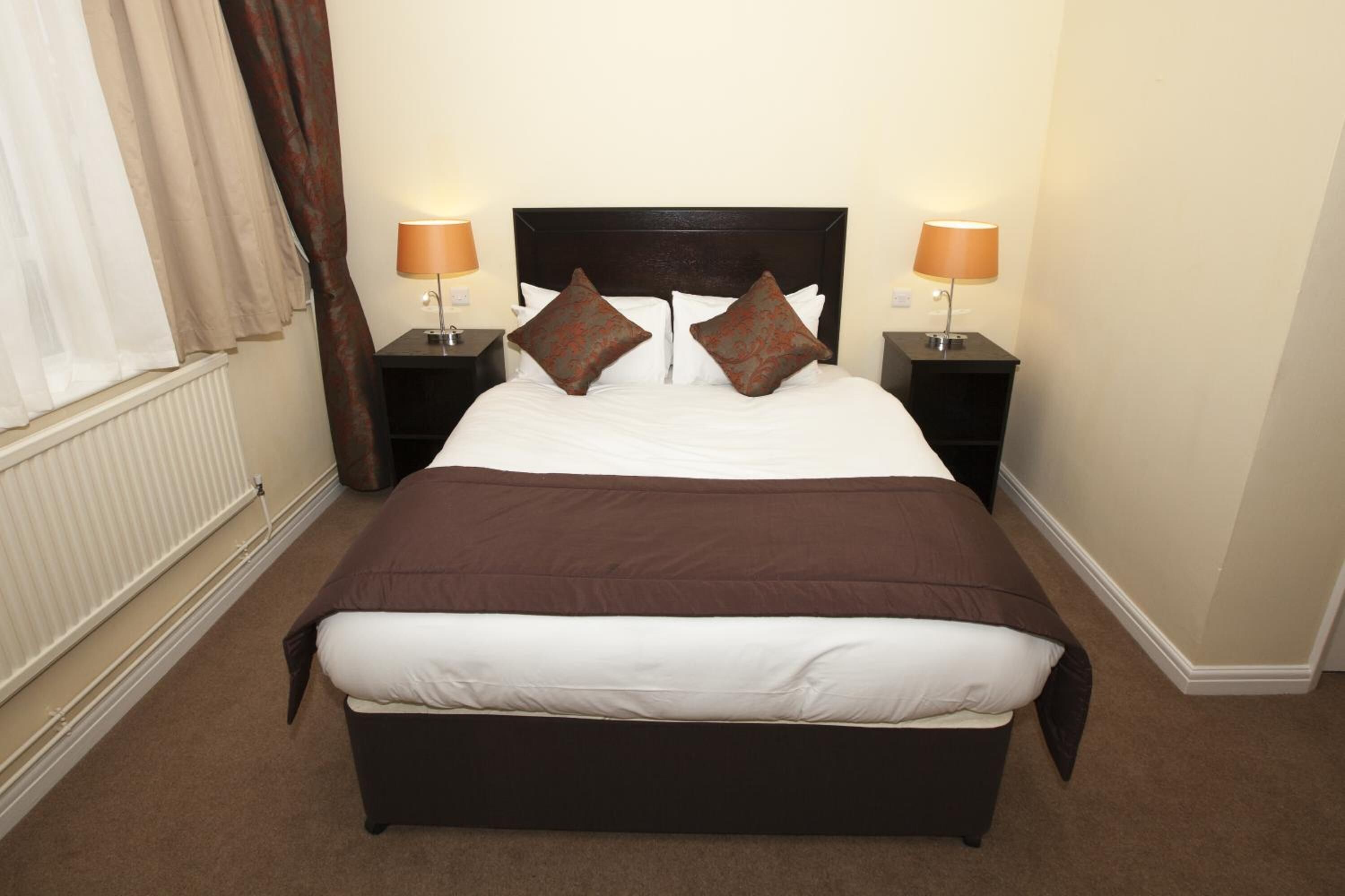 A standard hotel room with a large bed, two bedside tables with lamps, and a window with curtains.