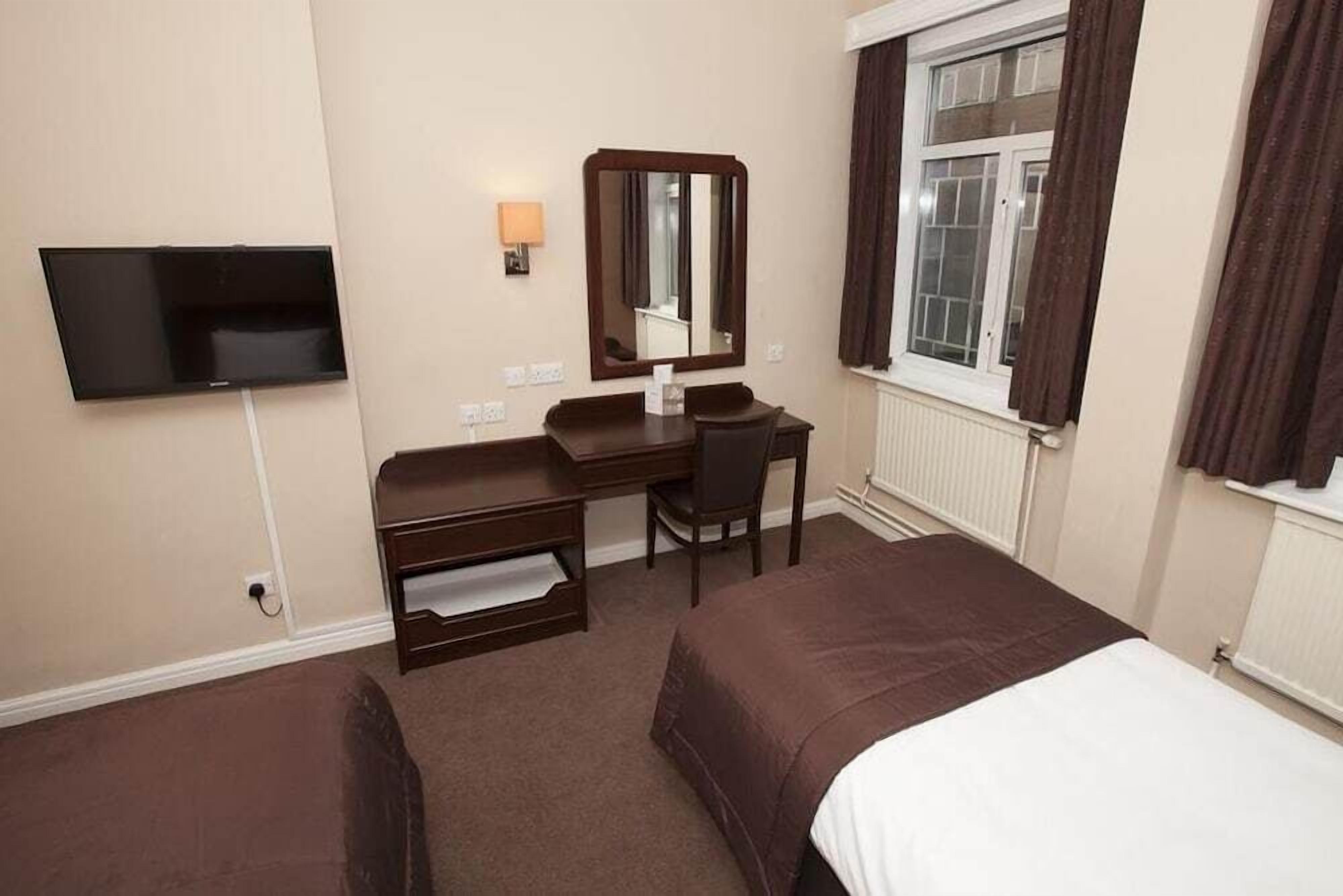 Une chambre d’hôtel avec deux lits, un bureau, une chaise, une télévision et une fenêtre avec des rideaux.