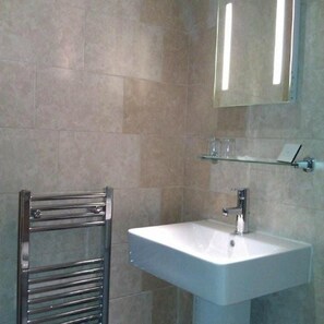 Un baño con toallero de cromo, lavamanos blanco y espejo sobre él.