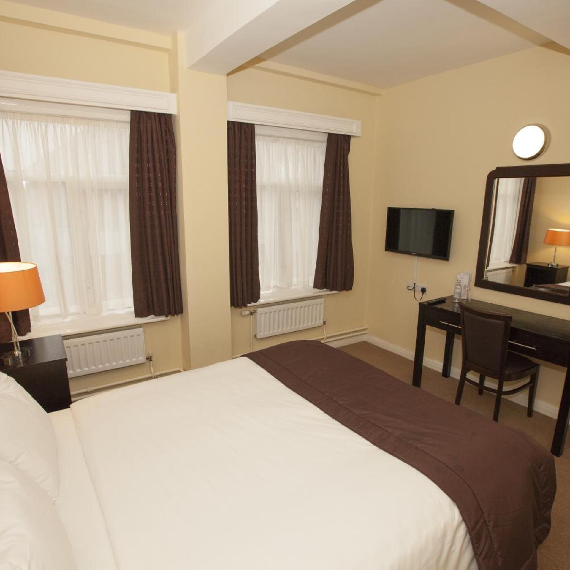 A hotel room with a large bed, a desk, a chair, a television, and a mirror.