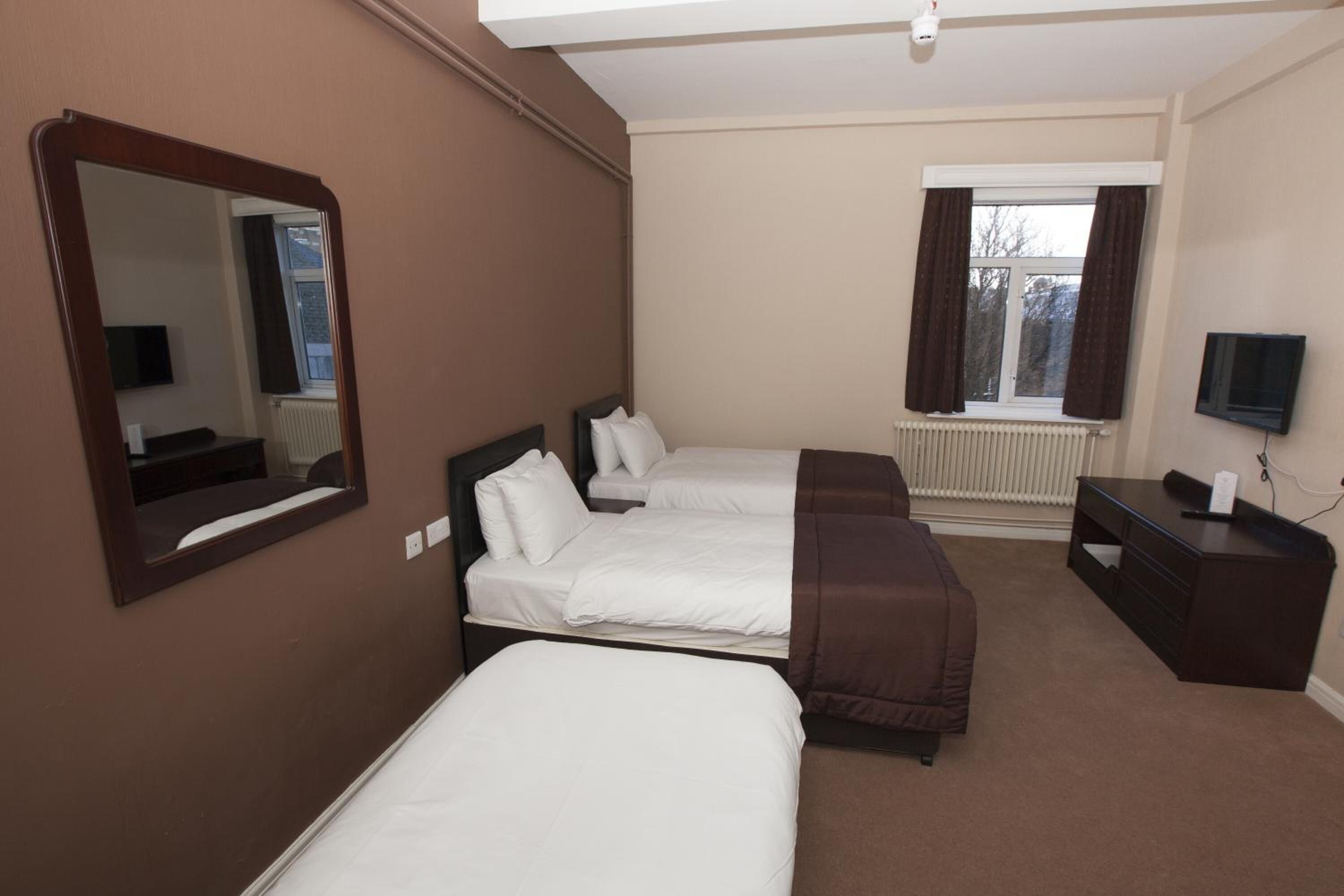 Een hotelkamer met drie bedden, een bureau, een spiegel en een televisie.