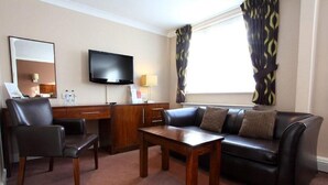 A hotel room with a sofa, a chair, a coffee table, a TV, and a window with curtains. - Dolphin Sa1 (Swansea)