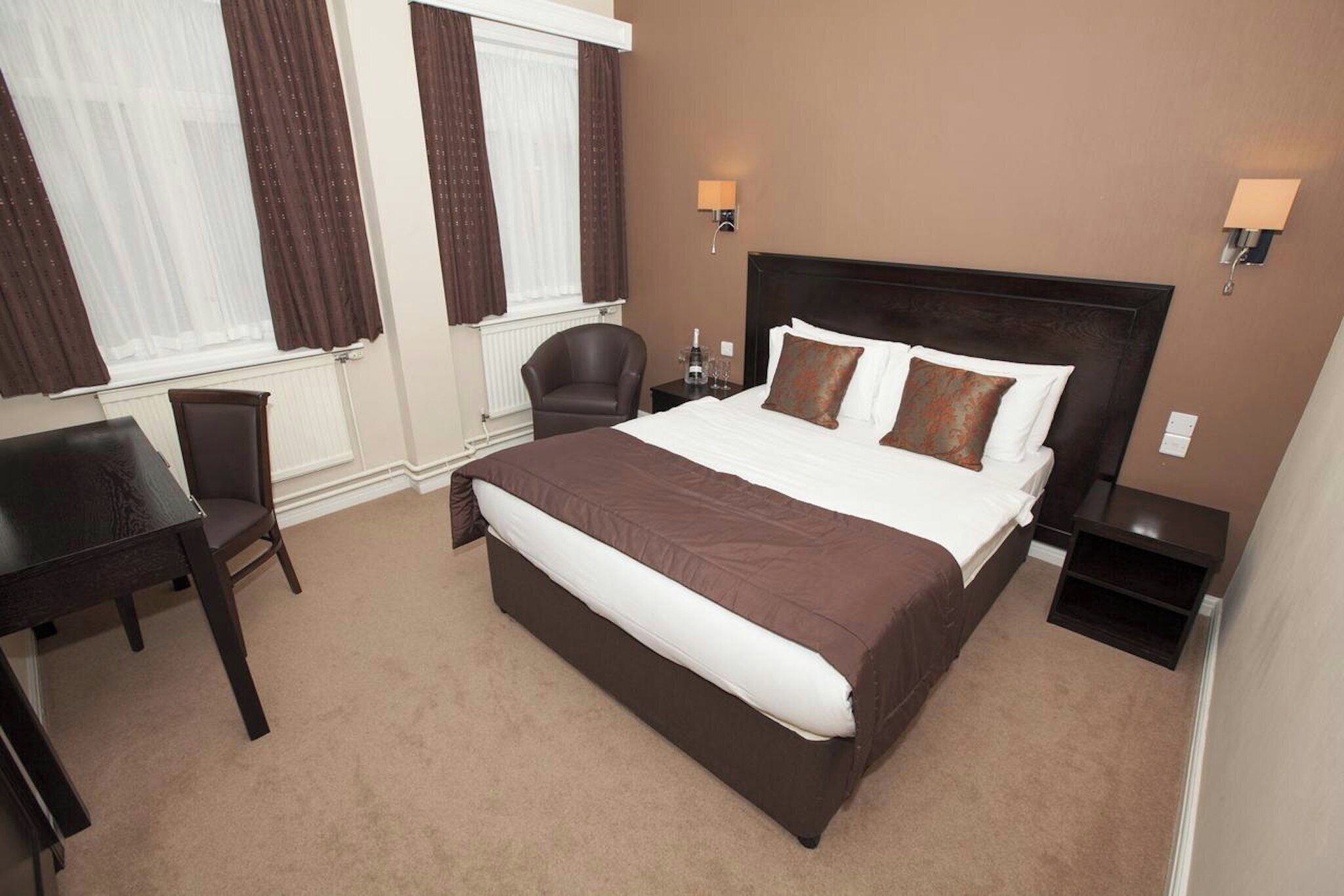 A hotel room with a large bed, two bedside tables, a chair, and a desk.