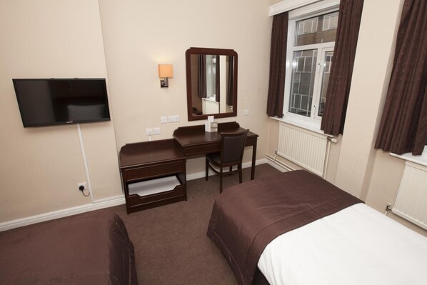 A hotel room with a bed, a desk, a chair, a television, a mirror, and a window with curtains. - Dolphin Sa1 (Swansea)