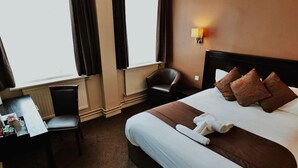 A hotel room with a bed, a desk, a chair, a lamp, and a window with curtains. - Dolphin Sa1 (Swansea)