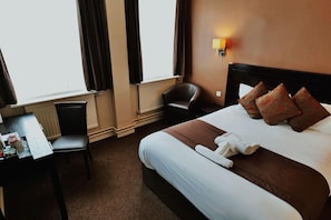 A hotel room with a bed, a desk, a chair, a lamp, and a window with curtains.