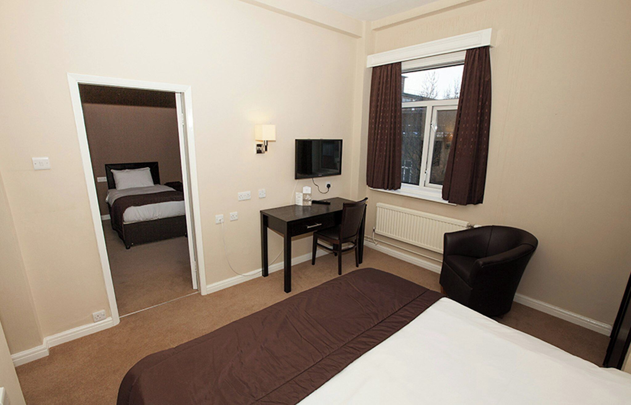 A hotel room with a bed, a desk, a chair, a television, and a window with curtains.