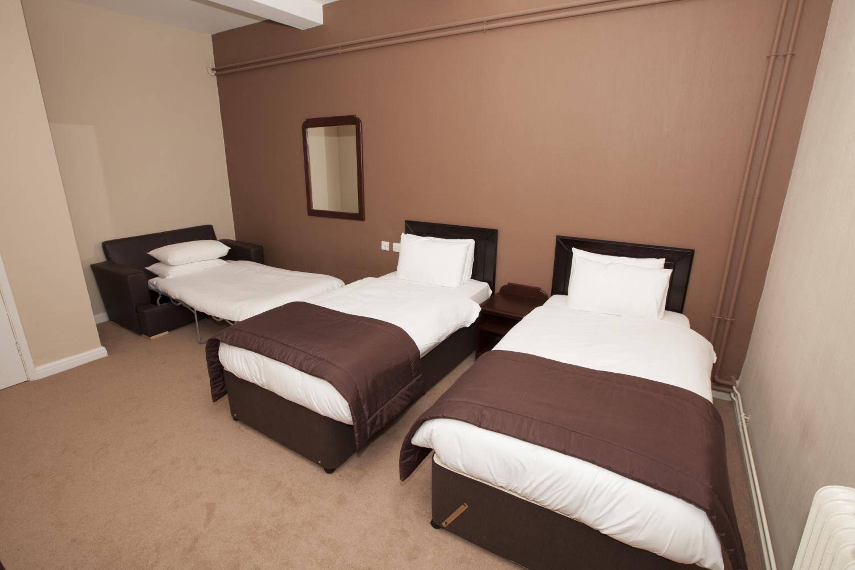 A hotel room with three beds, a bedside table, a mirror, and a carpeted floor.