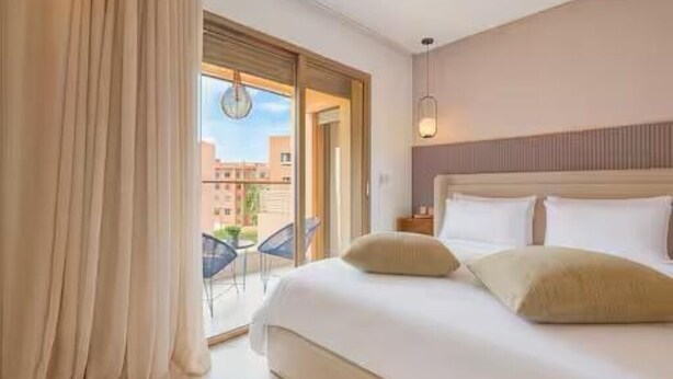 Ein Hotelzimmer mit Bett, Nachttisch, Lampe und Blick nach draußen.