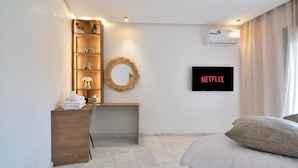 Ein Hotelzimmer mit Bett, Schreibtisch mit Stuhl, Wandfernseher, Ablagefläche mit Dekoration und Klimaanlage.