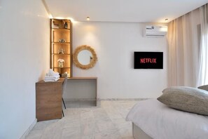 Ein Hotelzimmer mit Bett, Schreibtisch mit Stuhl, Wandfernseher, Ablagefläche mit Dekoration und Klimaanlage.