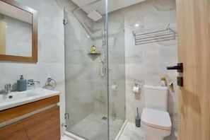 A modern bathroom with a glass shower enclosure, a toilet, and a vanity with a mirror. - Modern studio in the heart of Guéliz (Marrakech)