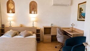 Camera da letto con un letto, comodini, una scrivania, una sedia, un condizionatore d'aria e opere d'arte appese al muro.