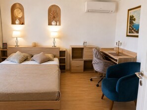 A bedroom with a bed, bedside tables, a desk, a chair, an air conditioner, and wall-mounted artwork. - 3-room apartment with garden near the sea (Nice)