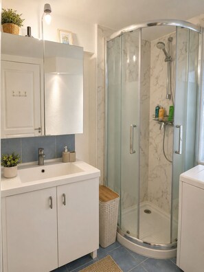A modern bathroom with a glass shower enclosure, white cabinetry, and a small trash bin. - 3-room apartment with garden near the sea (Nice)