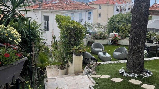 Un giardino con vialetto, piante in vaso e mobili da esterno.