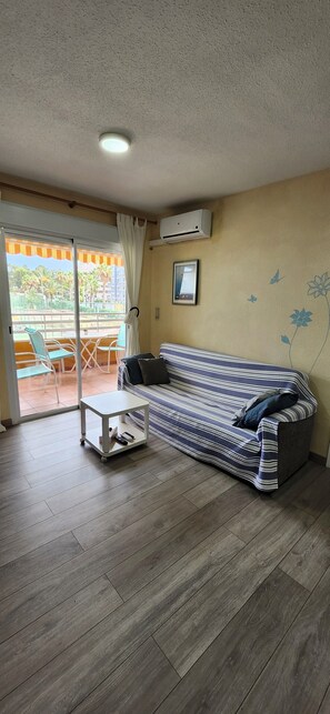 Ein Wohnzimmer mit einer Couch, einem kleinen Tisch, einer Schiebetür zu einem Außenbereich und einer Klimaanlage an der Wand.