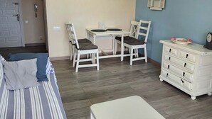 Una sala de estar con sofá, mesa de comedor con sillas, una mesita blanca y un aparador.