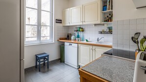 A kitchen with white cabinets, a window, a sink, and a toaster. - L'Heure Dorée - Duplex under the Grosse Horloge (La Rochelle)