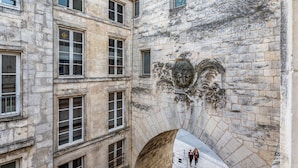 A stone building with multiple windows and a decorative emblem on the wall. - L'Heure Dorée - Duplex under the Grosse Horloge (La Rochelle)