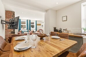 A dining area with a wooden table, chairs, and a TV mounted on the wall. - Harbour Cottage Seahouses (Seahouses)