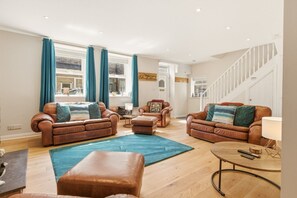 A spacious living room with leather sofas, a coffee table, and a large window with curtains. - Harbour Cottage Seahouses (Seahouses)