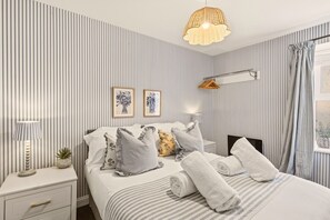 A hotel room with a striped wall, a bed with pillows, a bedside table with a lamp, and a hanging light fixture. - Harbour Cottage Seahouses (Seahouses)