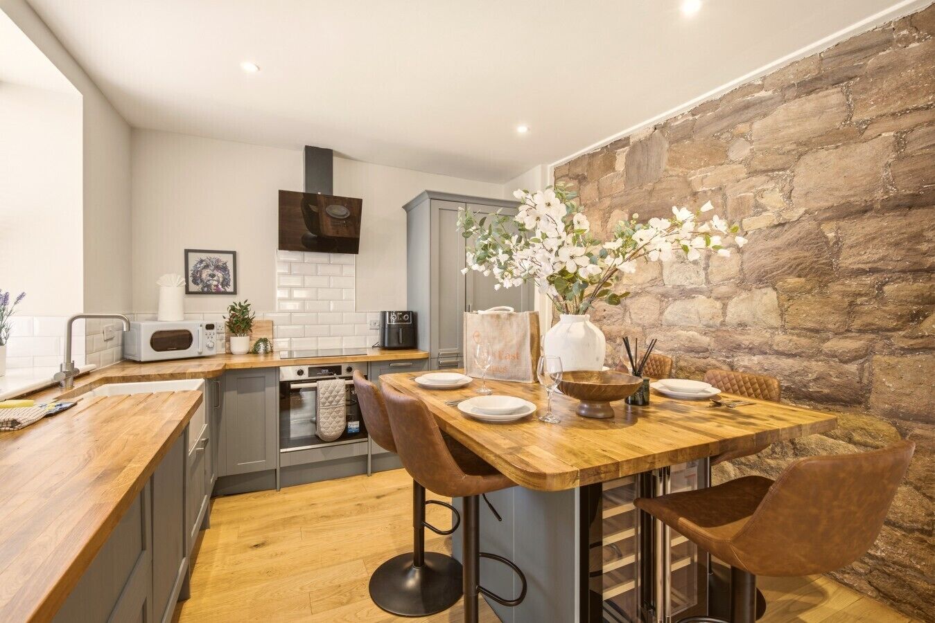 Une cuisine moderne avec une table à manger en bois, des tabourets de bar et un mur décoratif en pierre.